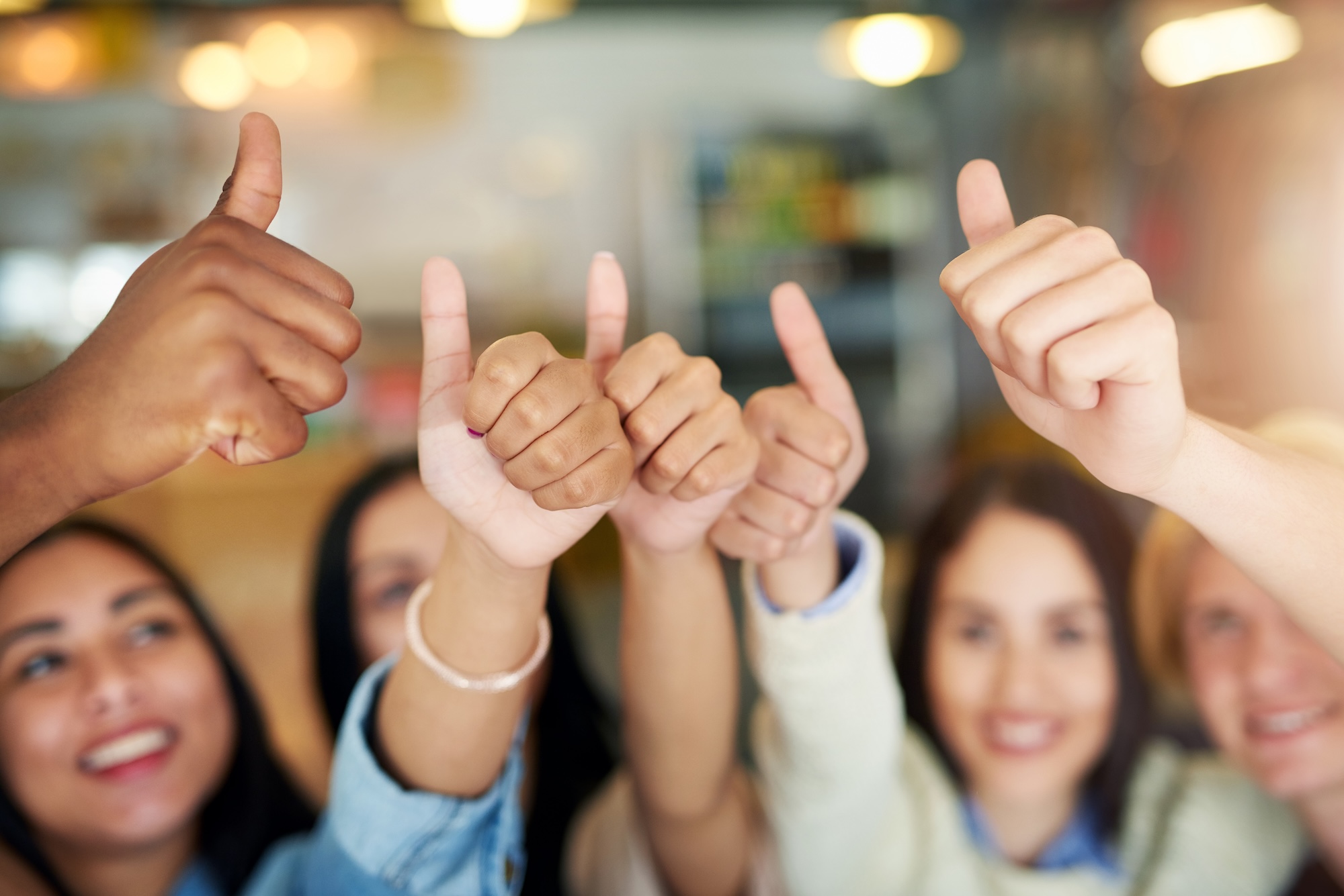 A group of people smiling and giving thumbs up gestures in a bright indoor setting, symbolizing positive customer testimonials. The focus is on their hands, with faces slightly blurred in the background.